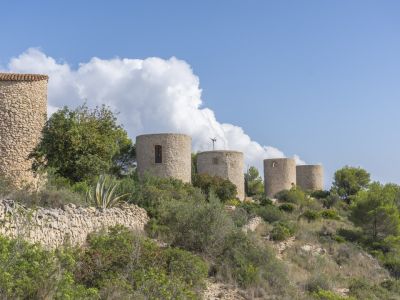 Blick auf die historischen Steinwindmühlen in Jávea, eingebettet in die mediterrane Landschaft.