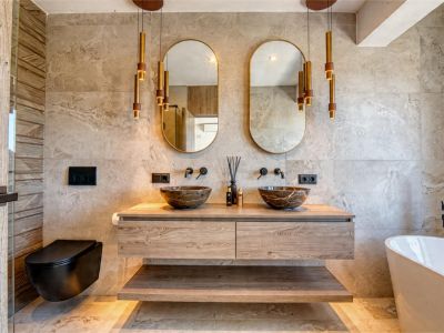 Elegantes Badezimmer mit Steinwaschbecken, schwebendem Waschtisch aus Holz und goldenen Pendelleuchten. Modernes Design mit neutralen Fliesen.