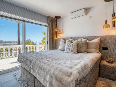 Helles Schlafzimmer mit Zugang zur Terrasse und Meerblick. Bett mit gepolstertem Kopfteil und neutraler Bettwäsche.
