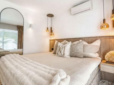 Schlafzimmer mit Holzkopfteil, goldener Pendelleuchte und Ganzkörperspiegel.
