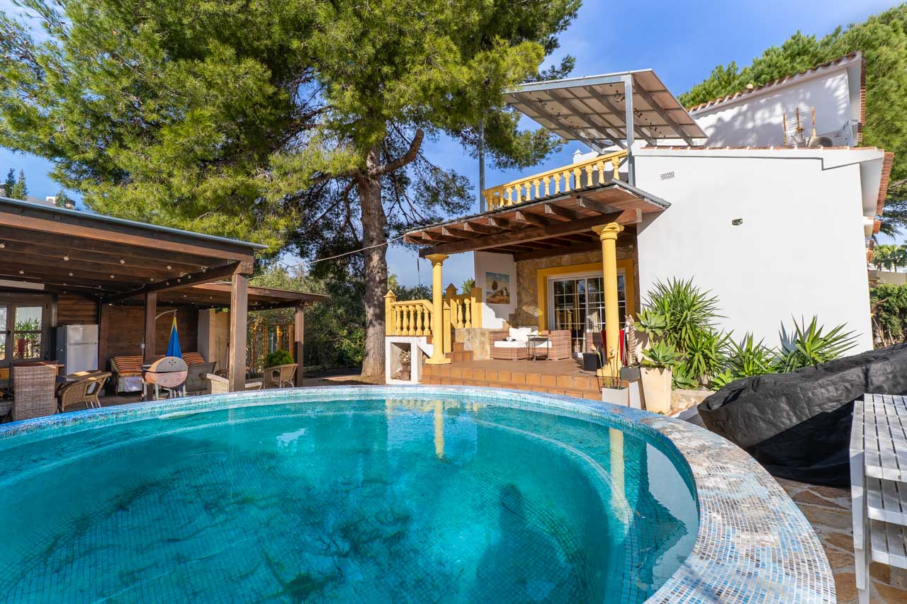 Ansicht des Pools mit blauen Mosaikfliesen und der überdachten Terrasse mit gelben Säulen.