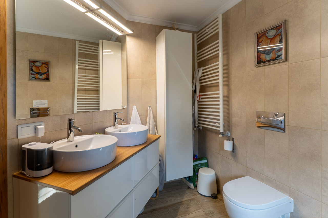 Badezimmer mit Doppelwaschbecken auf Holzarbeitsplatte, beheiztem Handtuchhalter und sandfarbenen Keramikfliesen.