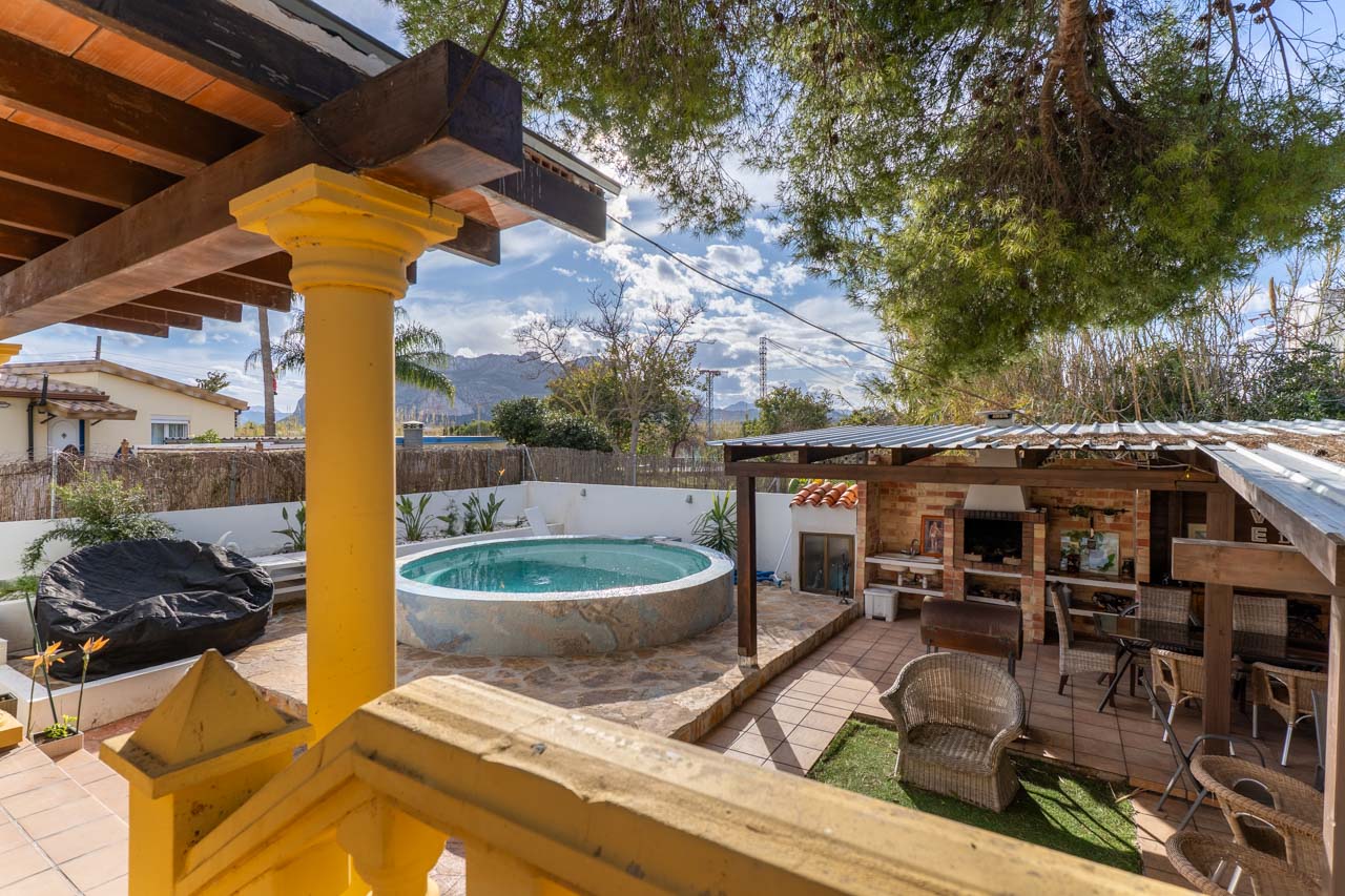 Blick vom Terrasse mit gelbem Geländer auf den Poolbereich mit überdachtem Grill.
