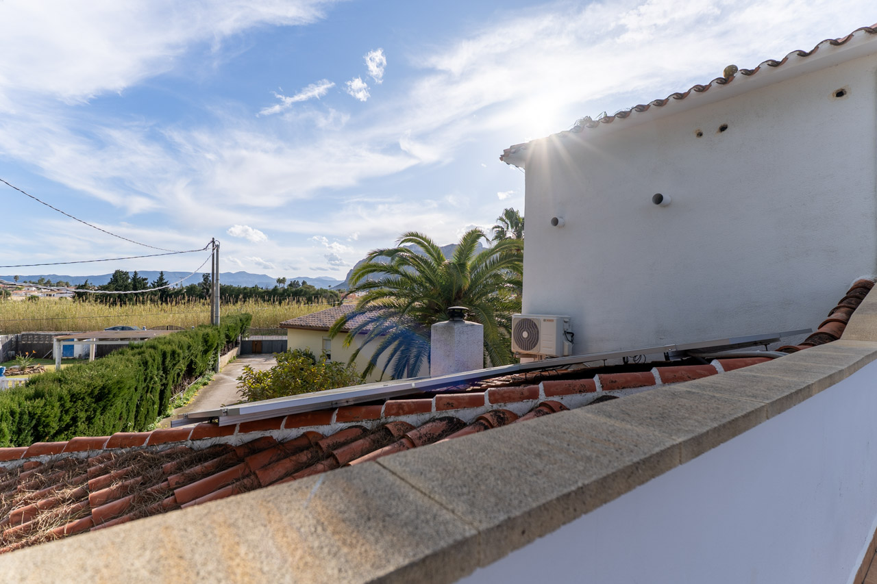 Blick von der Dachterrasse mit Tonziegeln und Solarpanel. Im Hintergrund Vegetation und Berge.