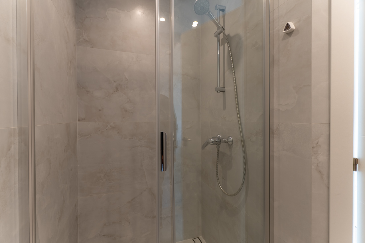 Detail der Dusche mit Glasabtrennung und Keramikfliesen in Marmoroptik.