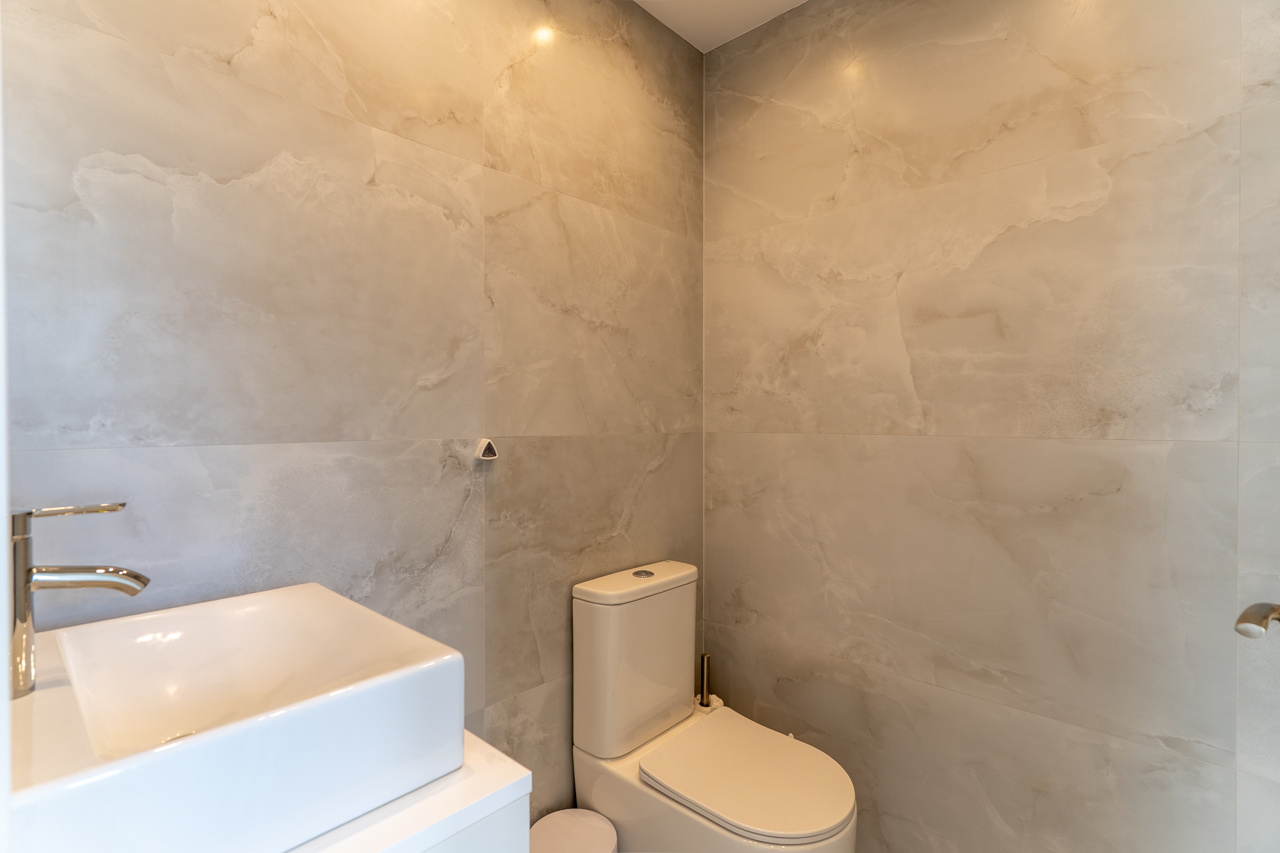 Detail eines modernen Badezimmers mit Wandfliesen in Marmoroptik, Aufsatzwaschbecken auf weißer Ablage und Toilette.