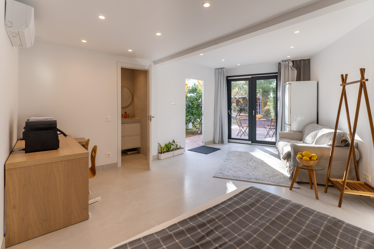 Heller, multifunktionaler Raum mit Gartenzugang, Bad en Suite und funktionalen Möbeln in neutralen Tönen.