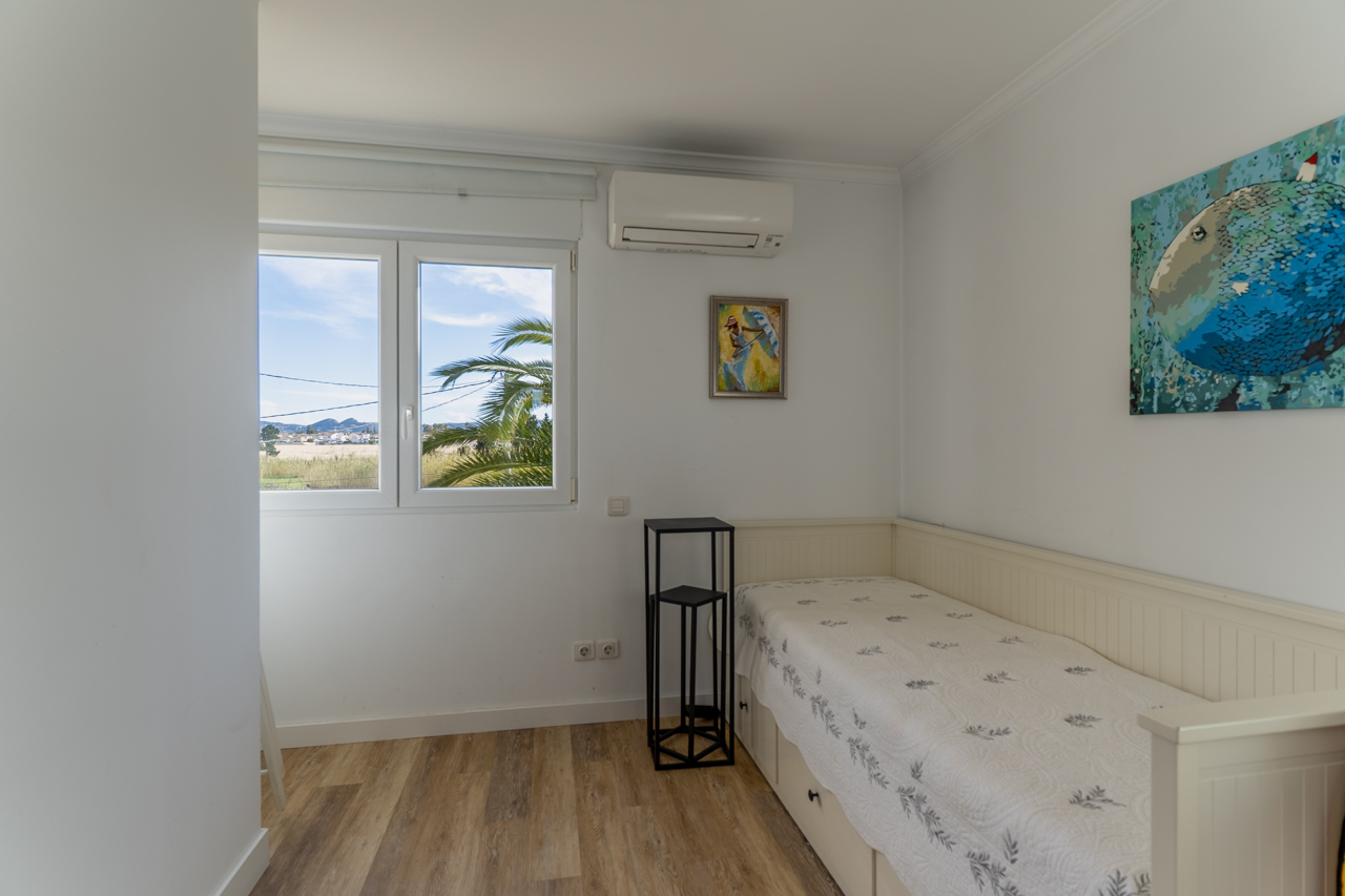 Helles Schlafzimmer mit Einzelbett, moderner Einrichtung und Außenansicht mit Palmen.