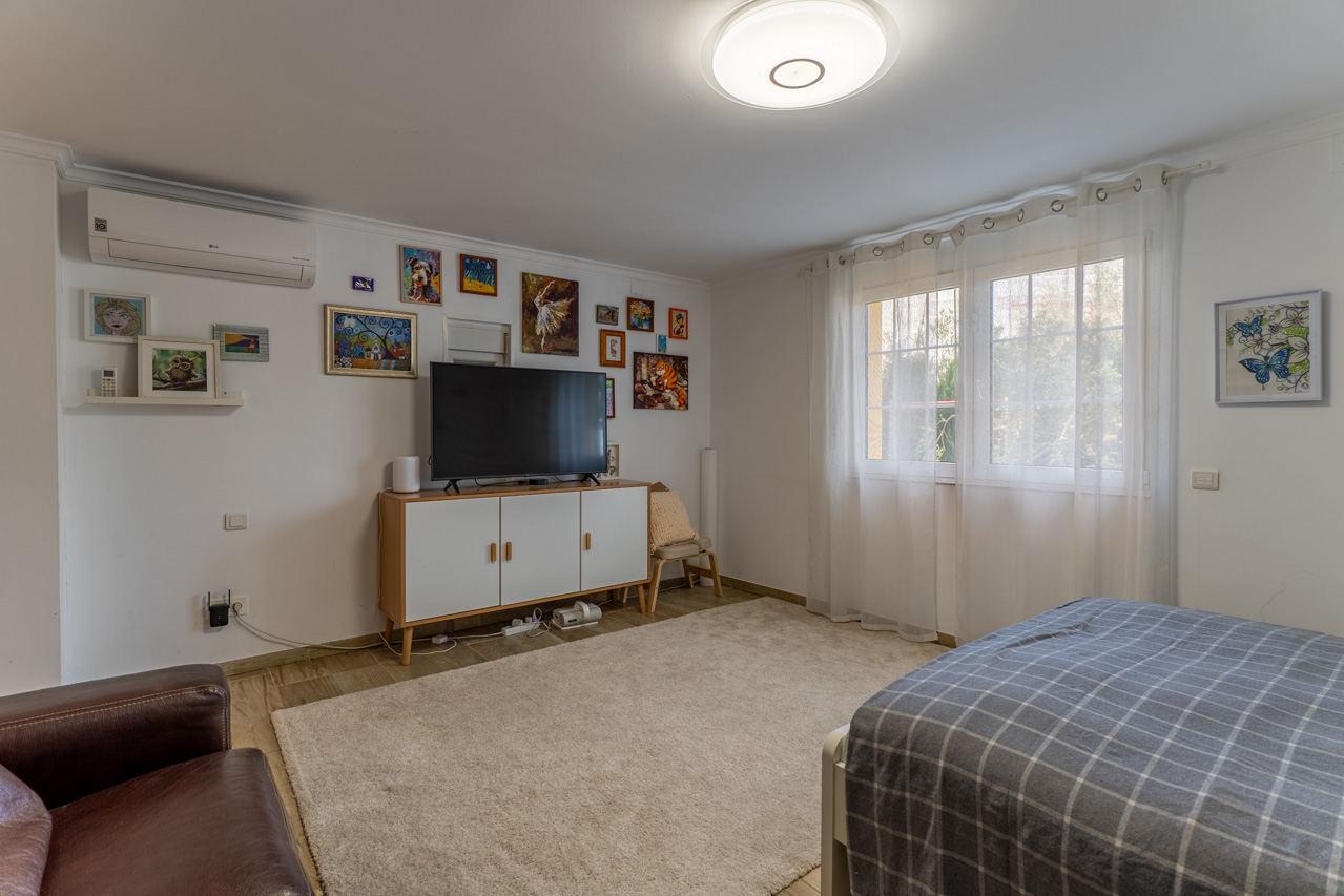 Helles Schlafzimmer mit flauschigem Teppich, weißem TV-Schrank und vielseitiger Kunst an der Wand.