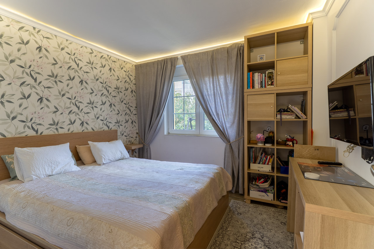 Helles Schlafzimmer mit floraler Tapete, hellem Holzbettrahmen und passenden modularen Regalen.