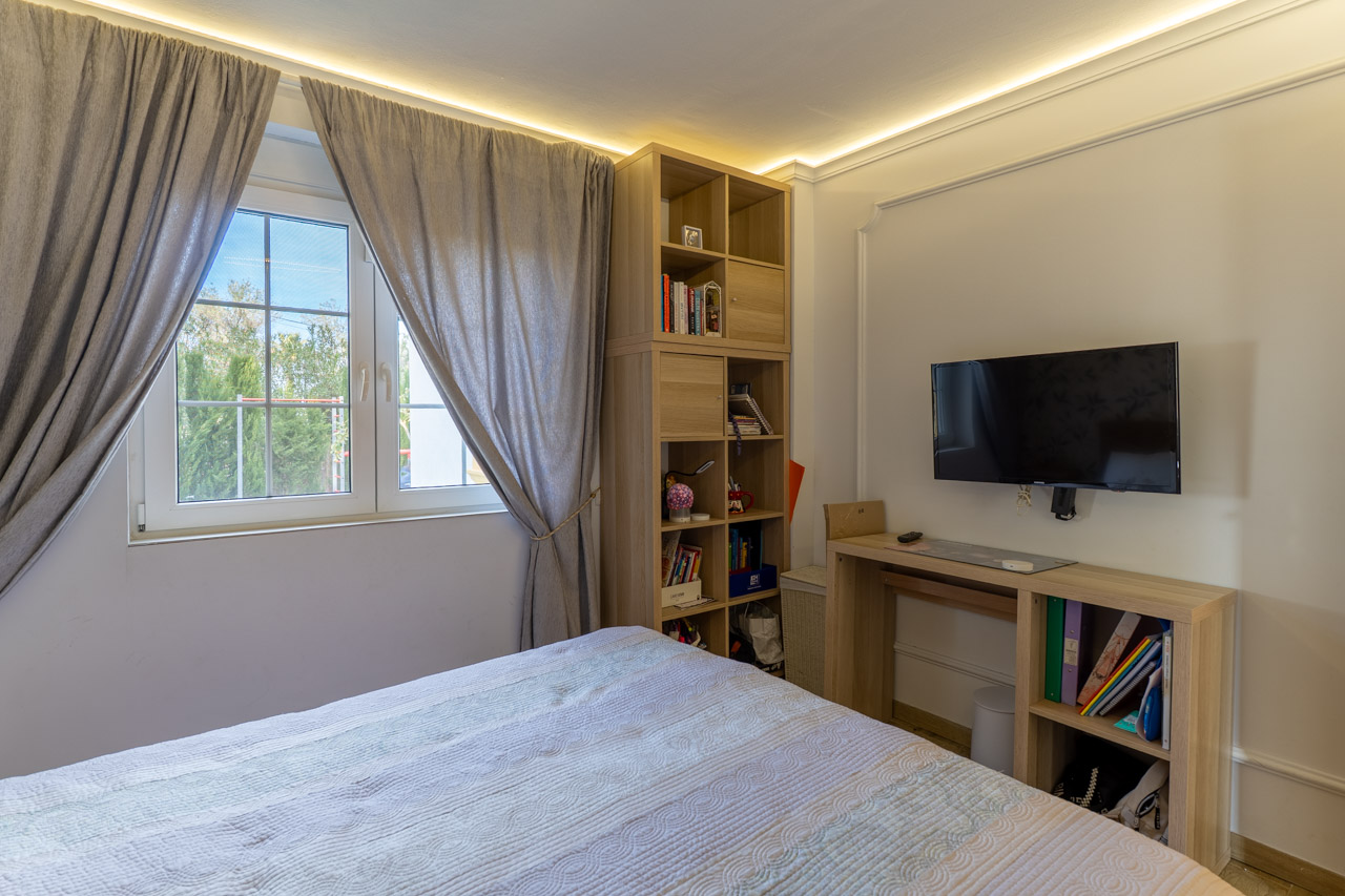 Helles Schlafzimmer mit hellem Holzregal und grauen Vorhängen neben einem Fenster.
