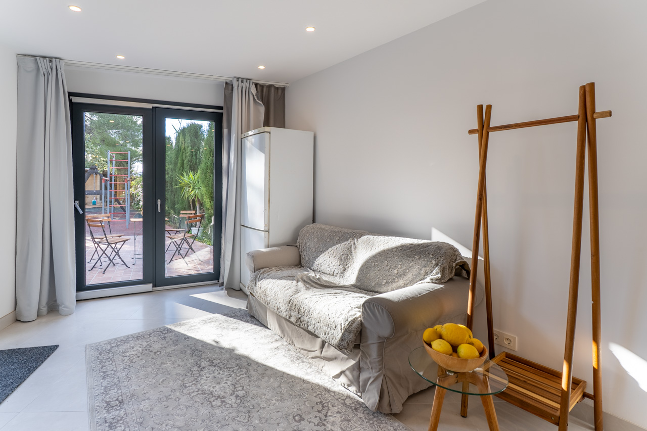 Helles Wohnzimmer mit abgedecktem Sofa, Zugang zur Terrasse und minimalistischem Dekor.