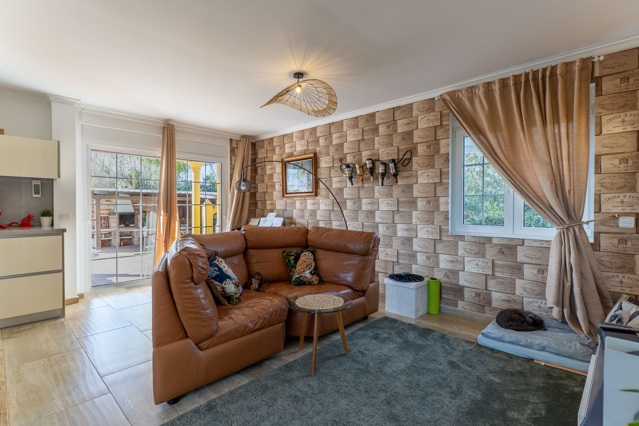 Helles Wohnzimmer mit Ledersofa, Weinkistenmotivtapete und Zugang zur Außenterrasse.