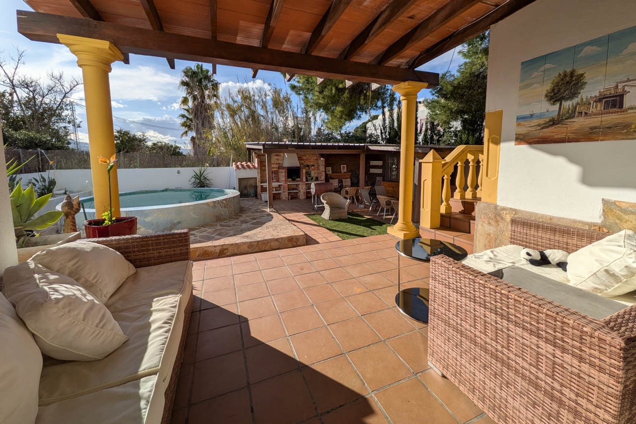 Terrassenansicht mit Pool, Grillplatz und überdachtem Sitzbereich mit Rattanmöbeln.