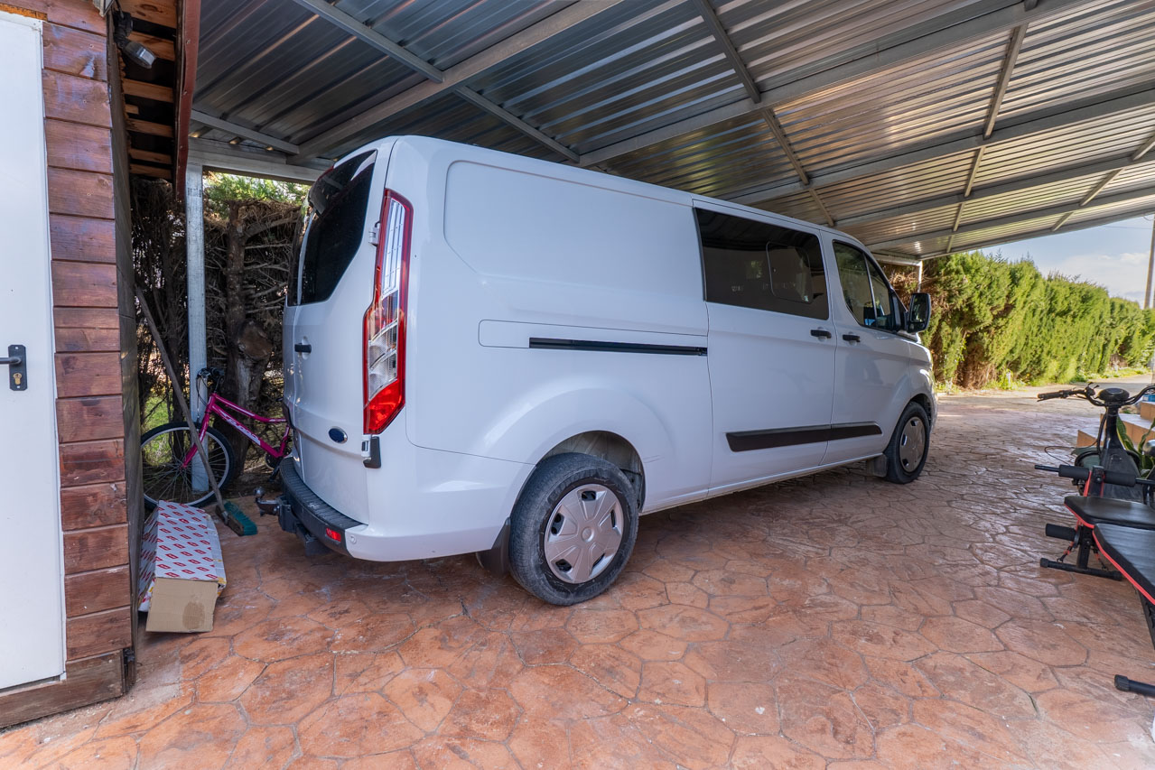 Überdachter Parkplatz mit weißem Transporter und geprägtem Steinboden.
