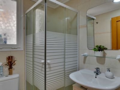 Badezimmerdetail mit Eckduschkabine und weißem Waschbecken mit rechteckigem Spiegel.