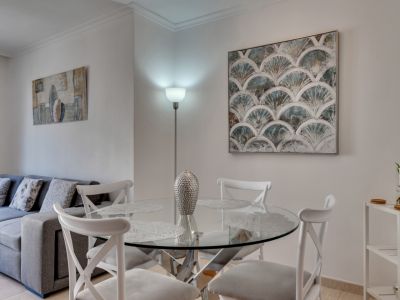 Heller Essbereich mit rundem Glastisch und weißen Stühlen, ergänzt durch moderne Kunst und einer Stehlampe.