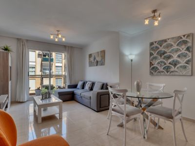 Heller Wohn-Essbereich mit Glastisch, grauem Ecksofa und Balkonzugang mit Stadtblick.
