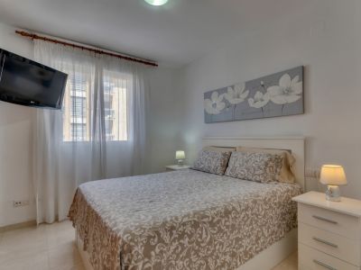 Helles Schlafzimmer mit Doppelbett, weißen Nachttischen und wandmontiertem Fernseher.