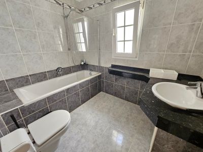 Badezimmer mit grauen Fliesen, Badewanne mit Glaswand und schwarzer Granit-Arbeitsplatte.