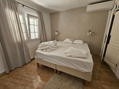 Schlafzimmer mit Doppelbett, Leinenvorhängen und rustikalem Fliesenboden.