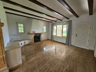 Wohnzimmer mit Steinkamin, Holzbalken und Fliesenboden.