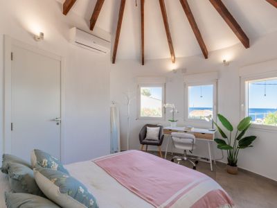 Helles Schlafzimmer mit gewölbter Decke mit Holzbalken und Schreibtisch mit Meerblick.