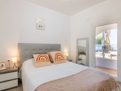 Helles Schlafzimmer mit grauem Kopfteil, weißer Bettwäsche und direktem Zugang zum Poolbereich.