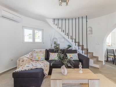 Helles Wohnzimmer mit grauem Sofa, Steintreppe mit schwarzem Geländer und hellem Holztisch.