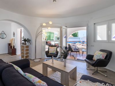 Helles Wohnzimmer mit Zugang zu Terrasse und Pool. Details wie die Bogenlampe und Blumenkissen bereichern den Raum.