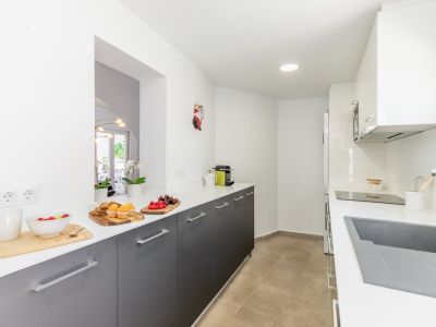Küchendetail mit weißer Arbeitsplatte, grauen Schränken und Keramikboden. Einbauleuchten.