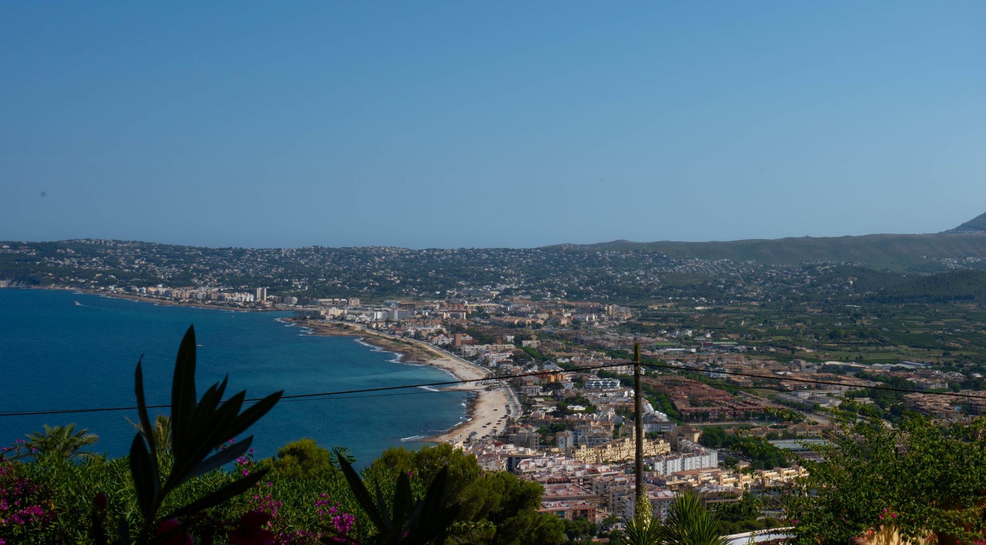 Panoramablick auf die Bucht von Jávea vom Grundstück aus, mit Vegetation im Vordergrund.