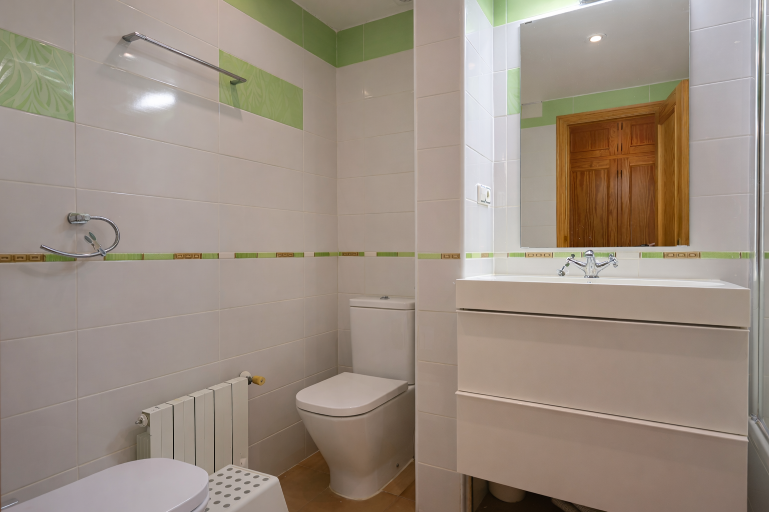 Badezimmer mit weißen Fliesen, grünen Akzenten, modernem Waschtisch und Spiegel.