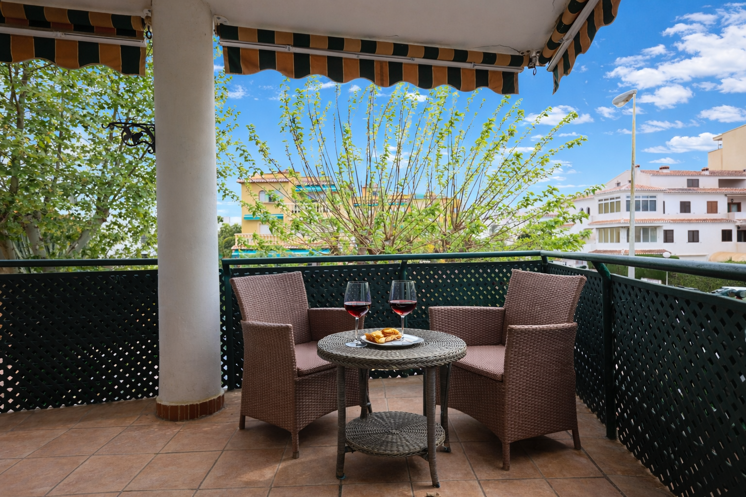 Geflieste Terrasse mit gestreifter Markise und Korbmöbeln mit Blick ins Freie.