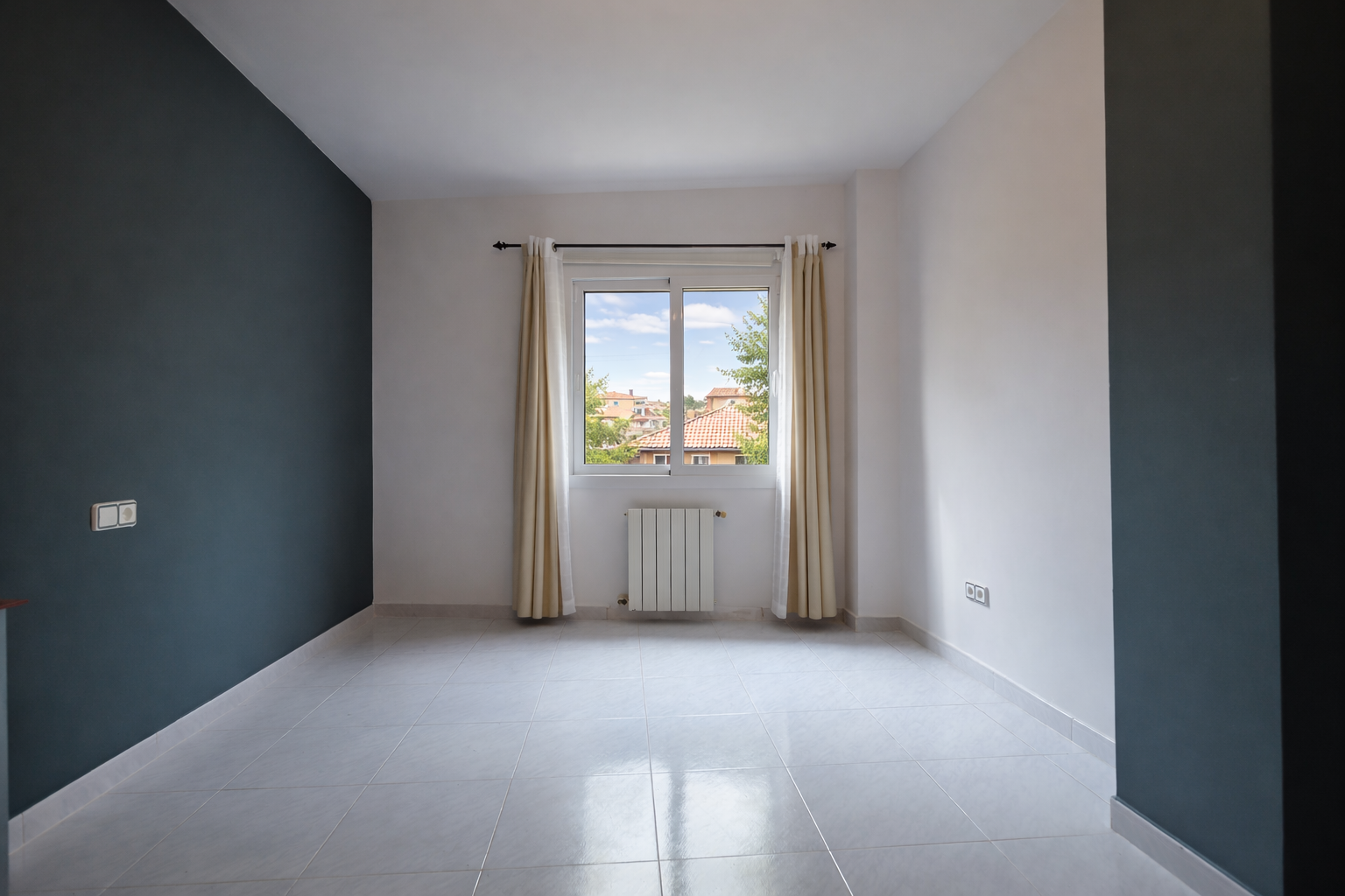 Heller Raum mit bleiblauer Akzentwand, Fenster mit Aussicht und Fliesenboden.