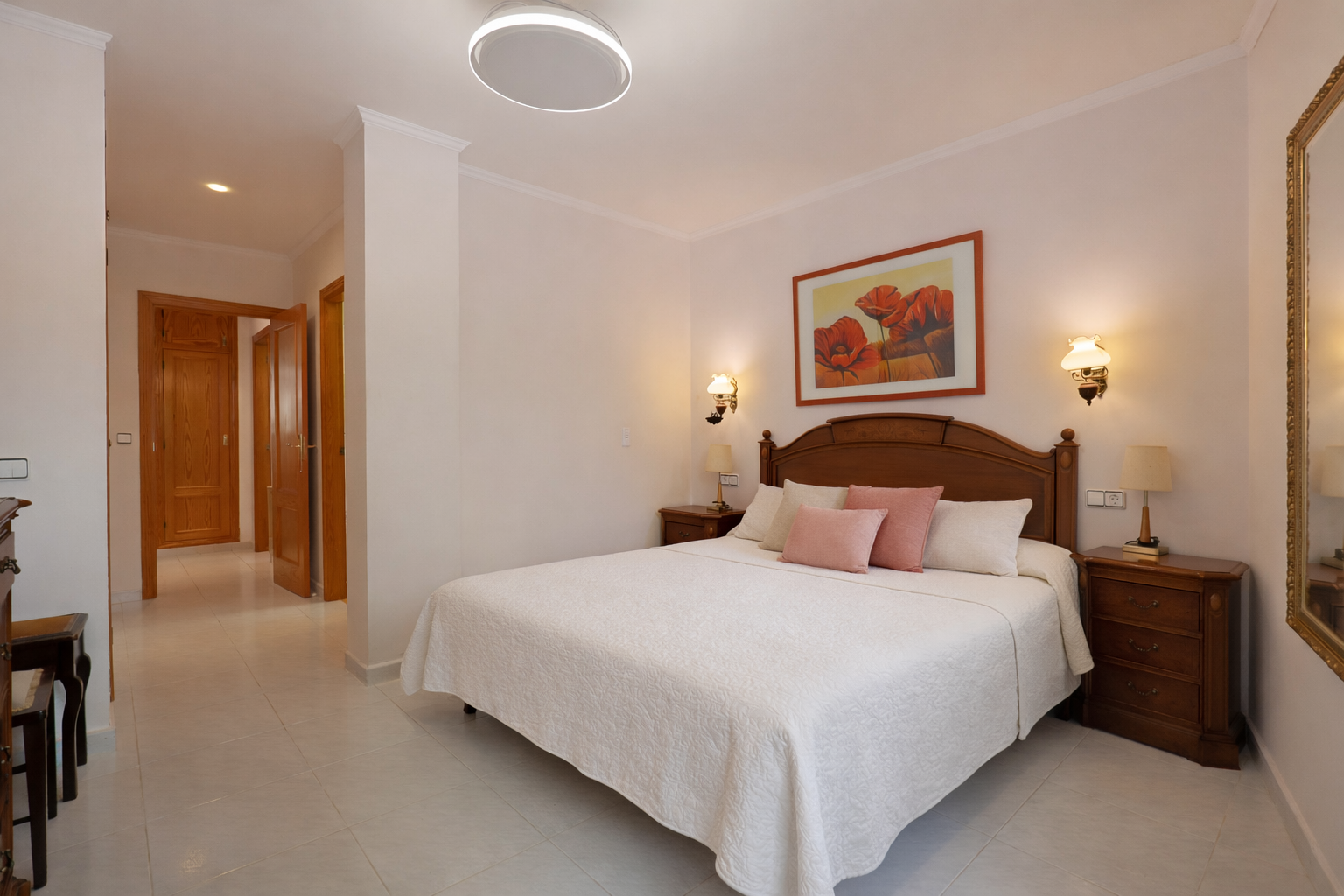 Helles Schlafzimmer mit Doppelbett, hölzernen Nachttischen und Fliesenboden.