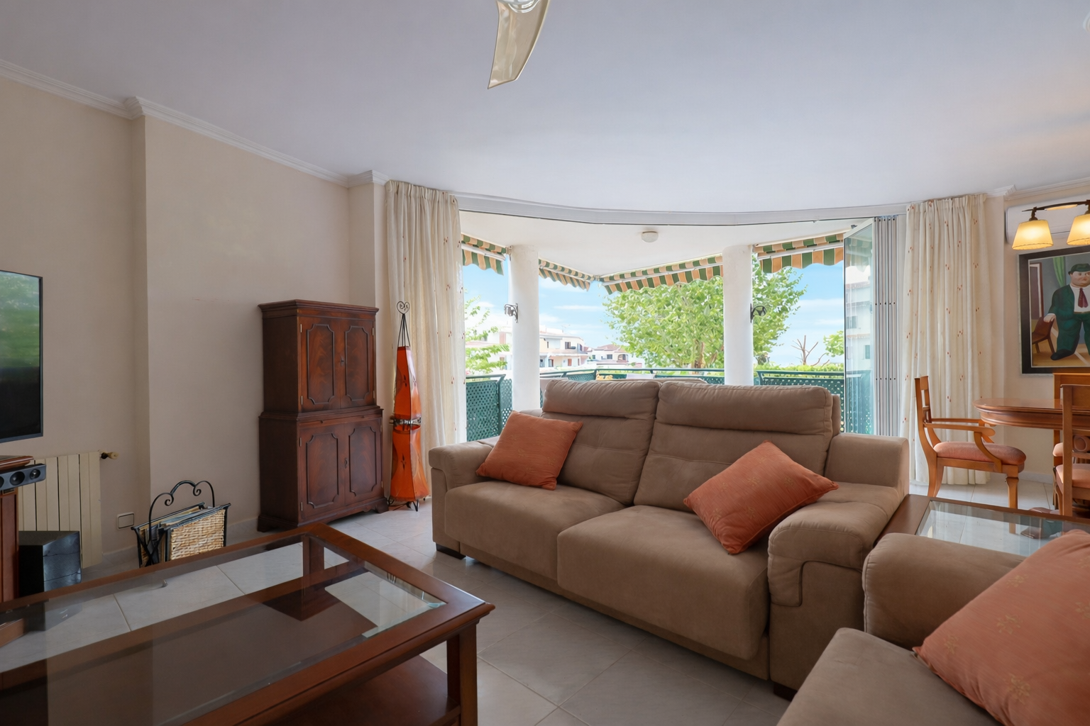 Helles Wohnzimmer mit Zugang zu einer überdachten Terrasse, möbliert mit beigem Sofa und Holzkaffeetisch.