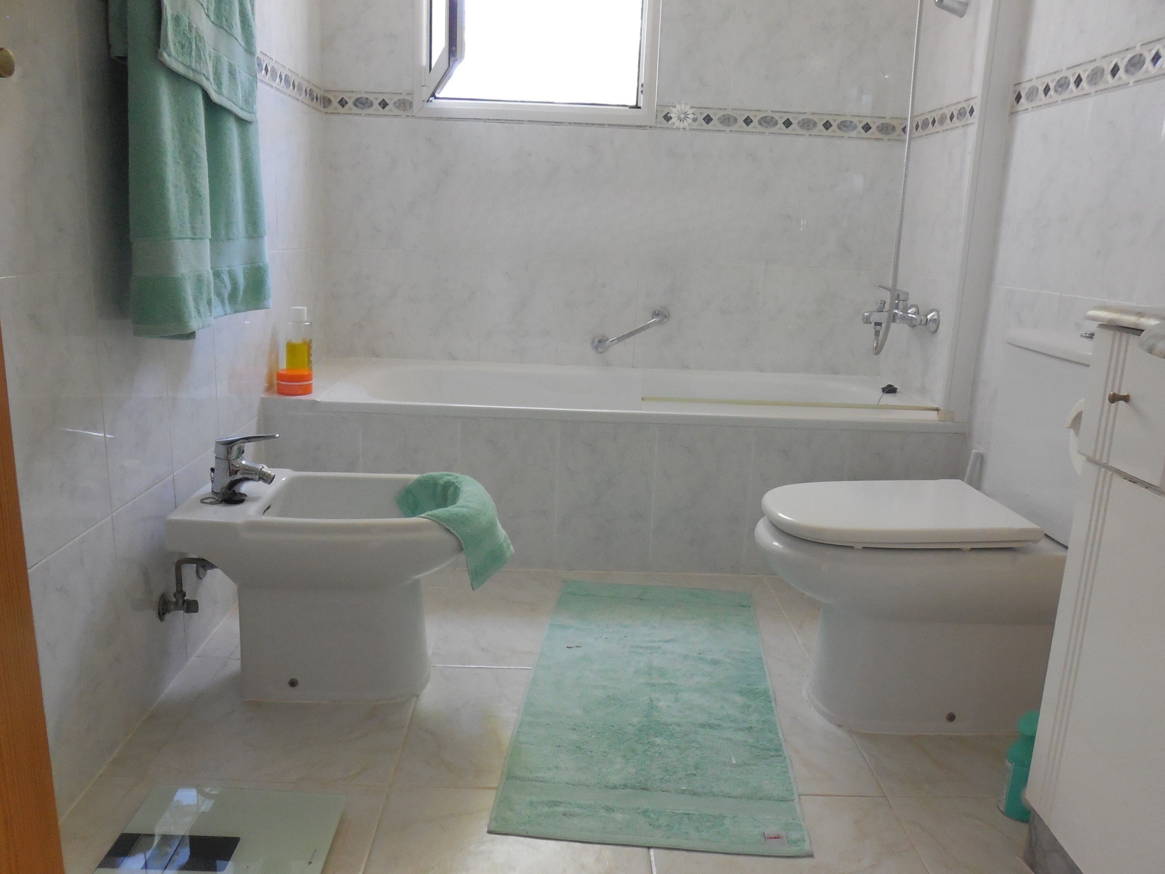 Badezimmer mit marmorähnlichen Fliesen, Badewanne, Bidet und mintgrünen Handtüchern.