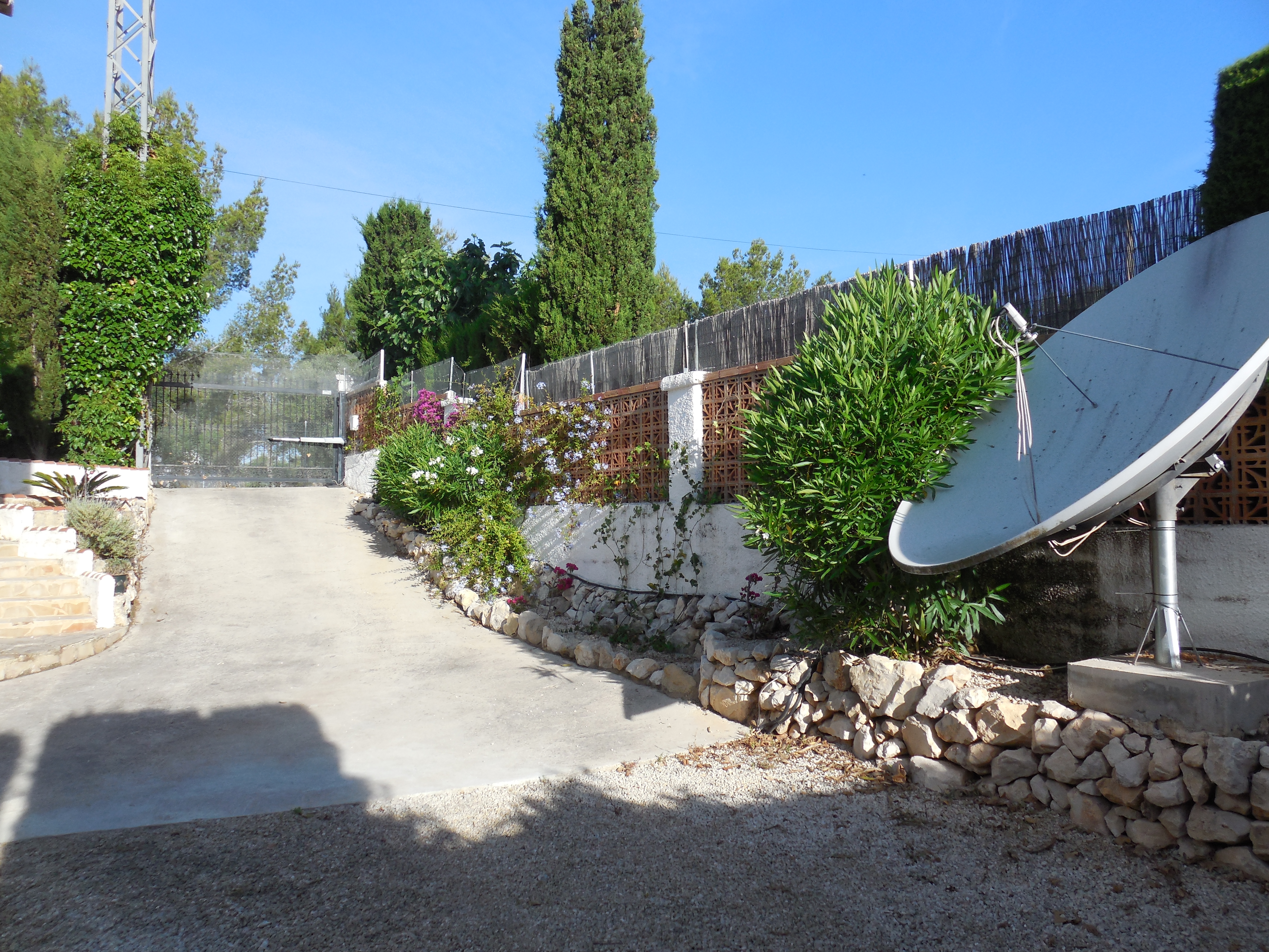Einfahrt zum Grundstück mit Betonweg, Backsteinzaun und üppigem Grün.