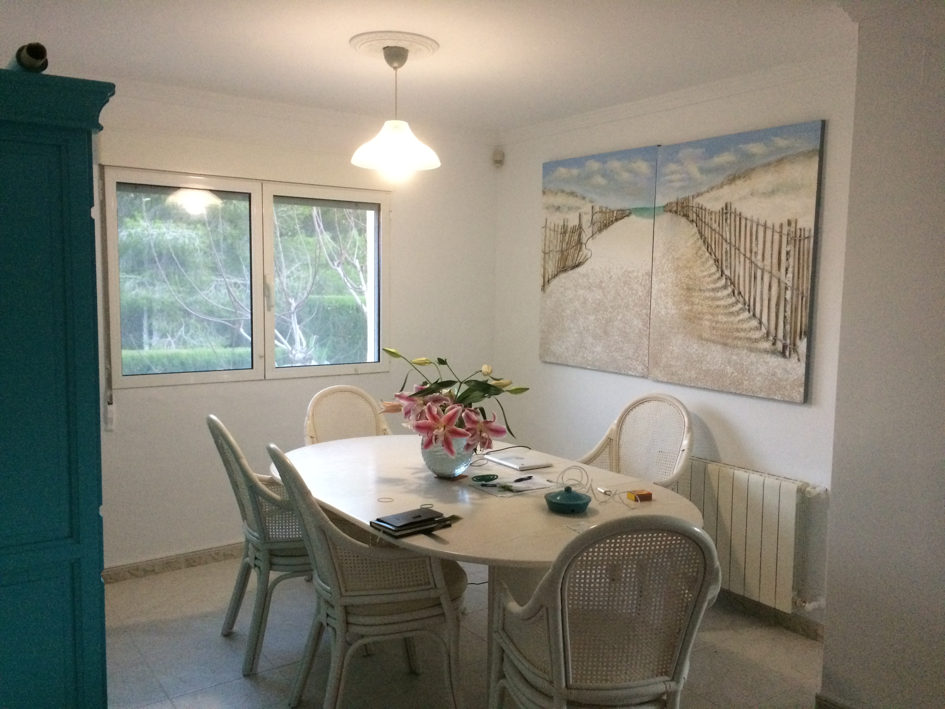 Heller Essbereich mit ovalem Steintisch, Korbstühlen und einem Gemälde mit Strandmotiv.
