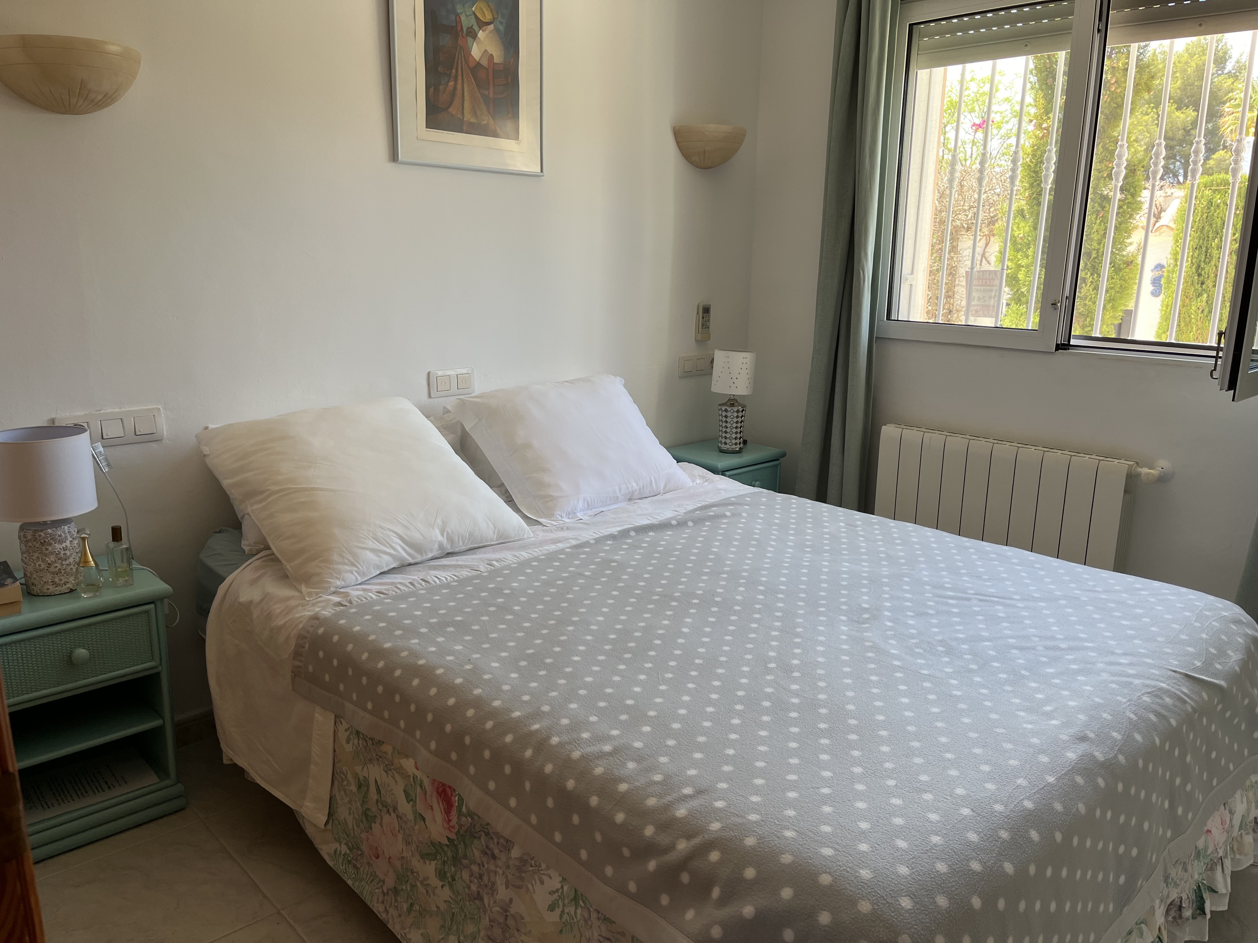 Helles Schlafzimmer mit Doppelbett, türkisfarbenem Nachttisch und dekorativen Details.