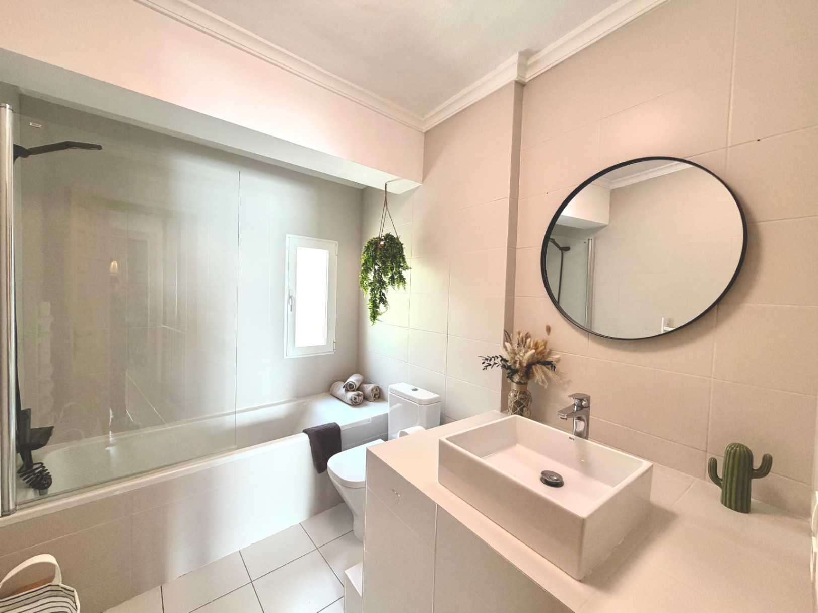 Detail des renovierten Badezimmers mit Badewanne, modernem Waschbecken, rundem Spiegel und dekorativen Elementen.