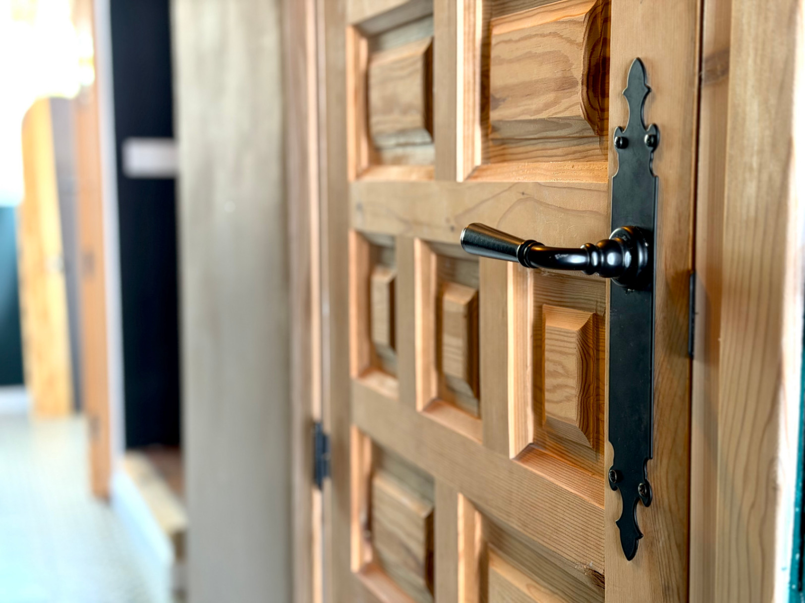 Detail einer Holztür mit Reliefdesign und einem schwarzen Schmiedeeisengriff.