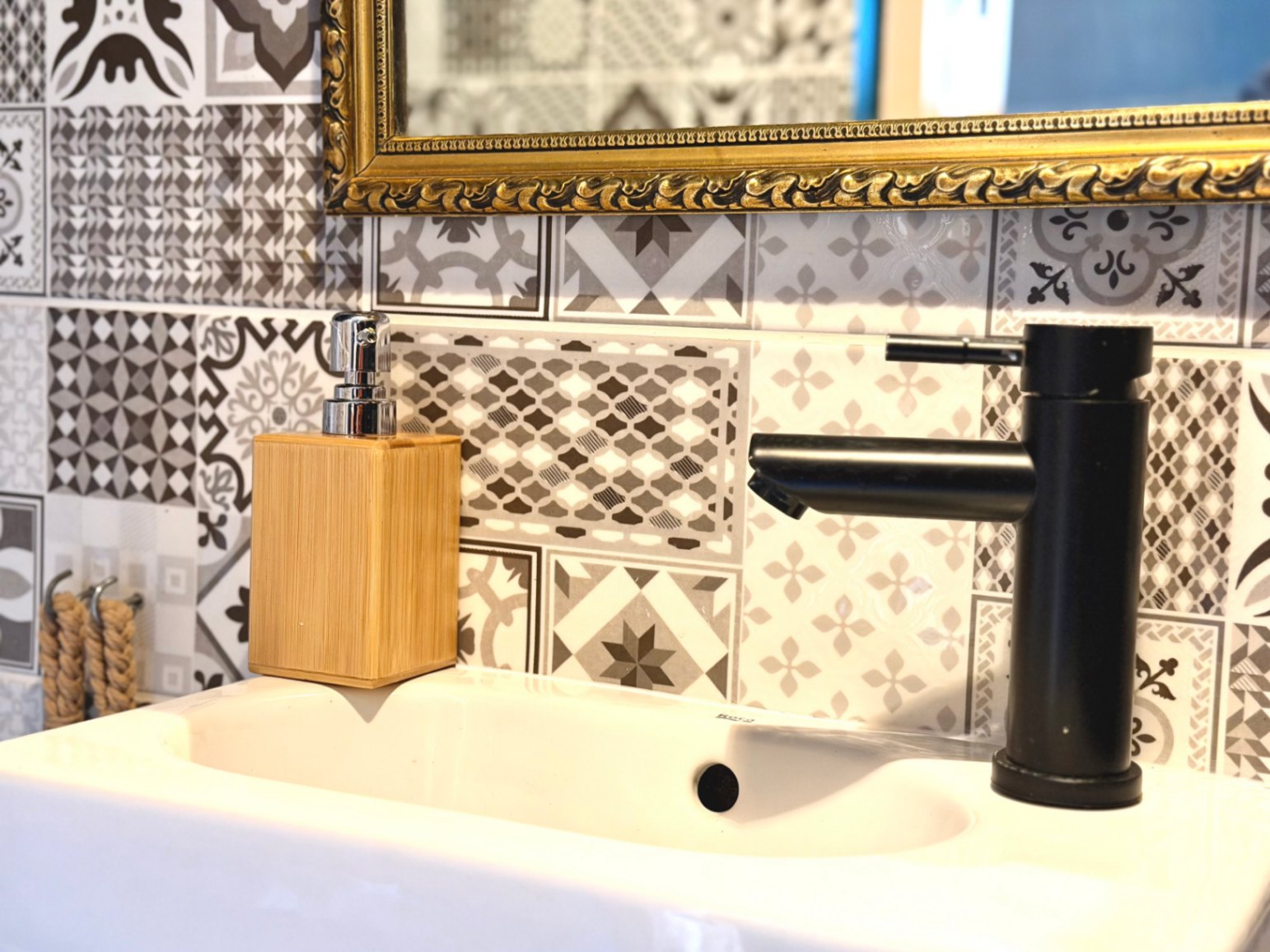 Detailansicht eines Waschbeckens mit mattschwarzem Wasserhahn und dekorativen Mosaikfliesen.