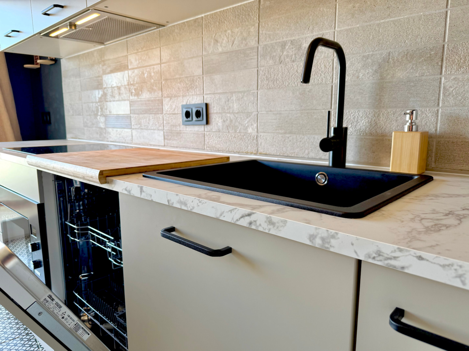 Detailaufnahme der renovierten Küche mit schwarzem Spülbecken, Marmorarbeitsplatte und strukturierter Fliesenrückwand.