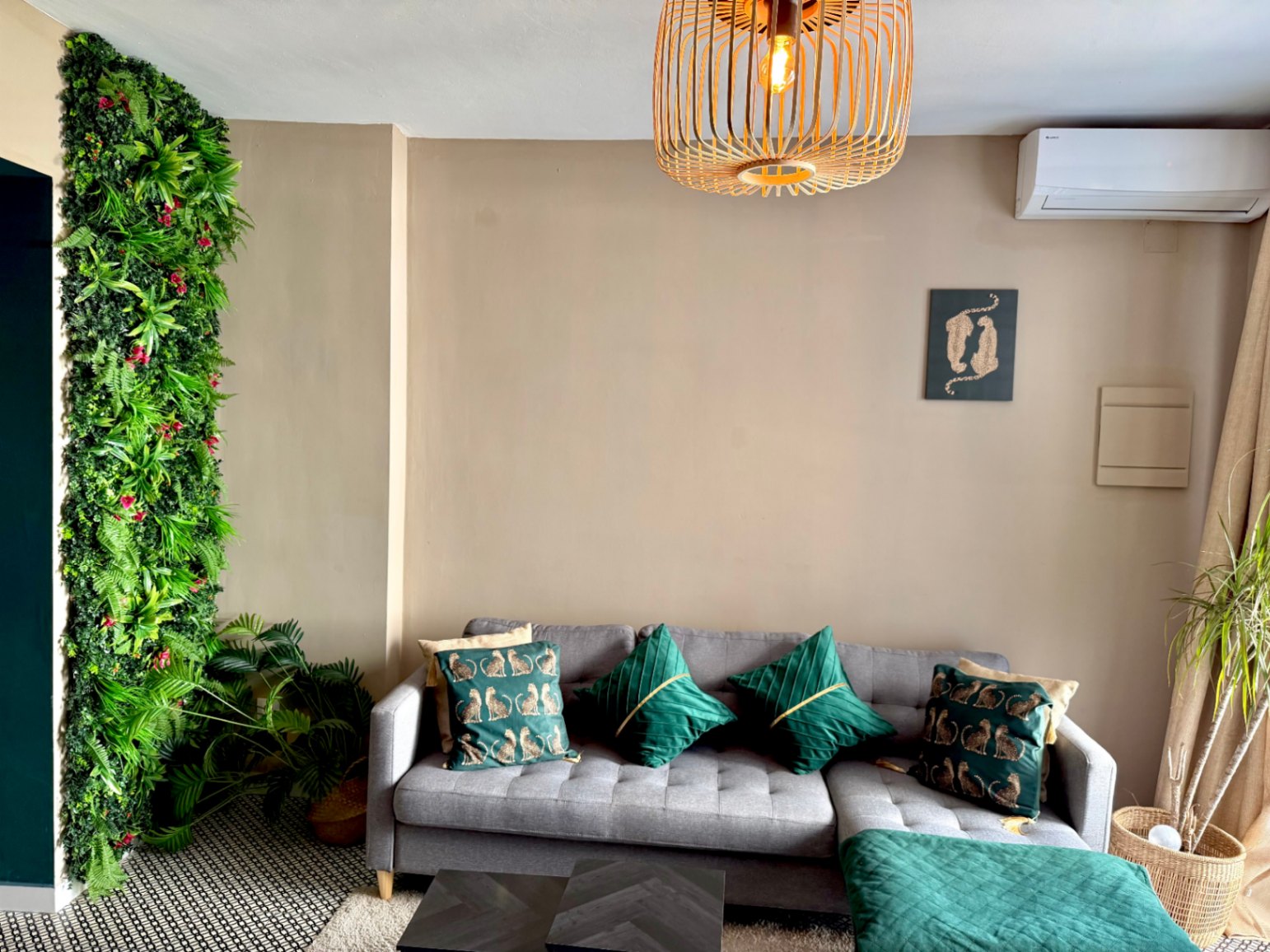 Helles Wohnzimmer mit vertikaler Grünwand, grauem Sofa mit Zierkissen und dunklem Couchtisch.