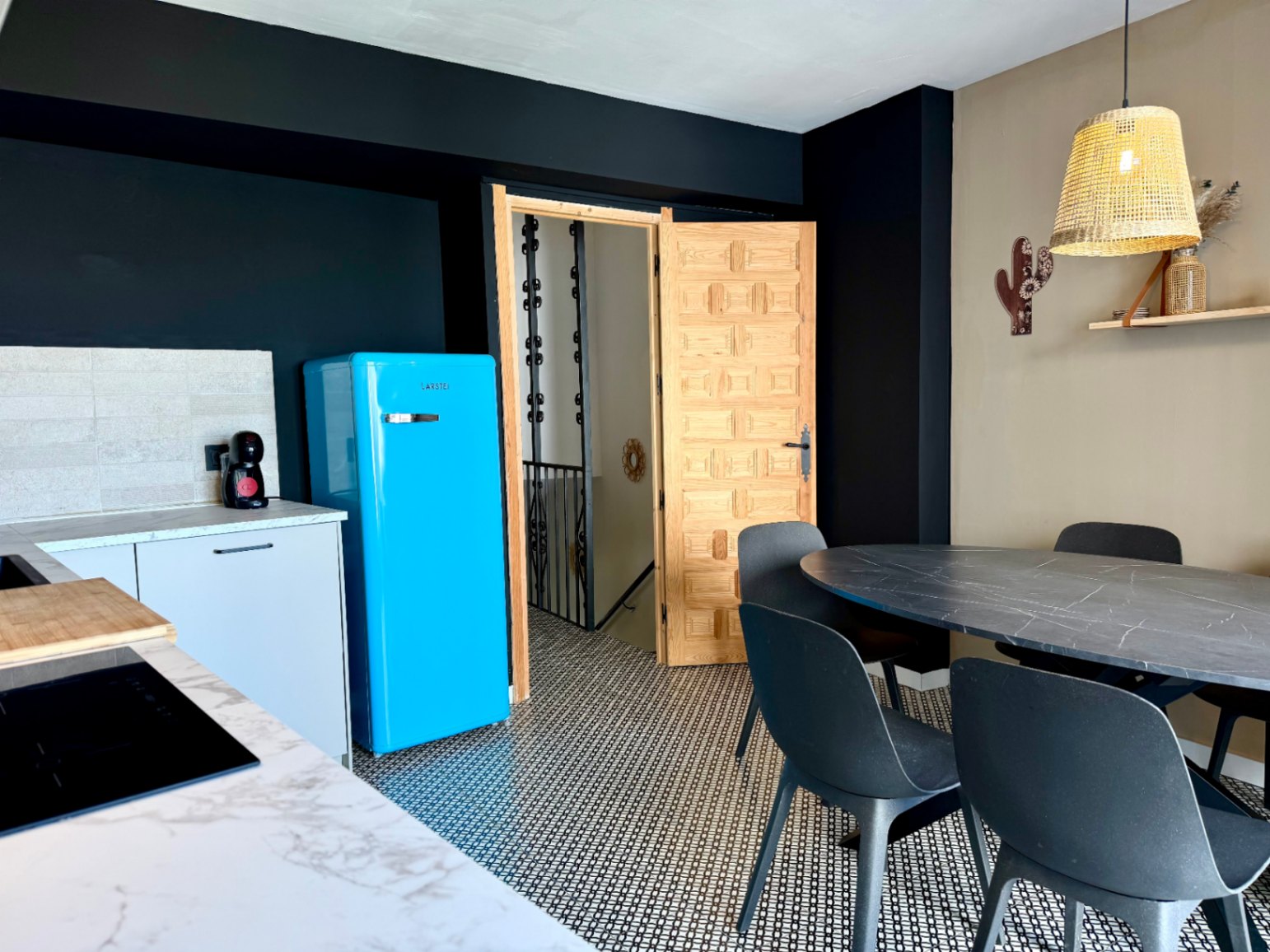 Küchendetail mit blauem Retro-Kühlschrank, ovalem Esstisch und geschnitzter Holztür.