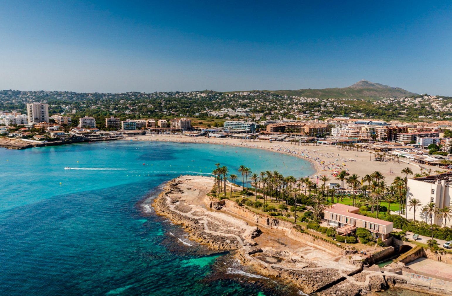 Luftaufnahme von Playa del Arenal in Jávea mit türkisfarbenem Wasser und Küstengebäuden.