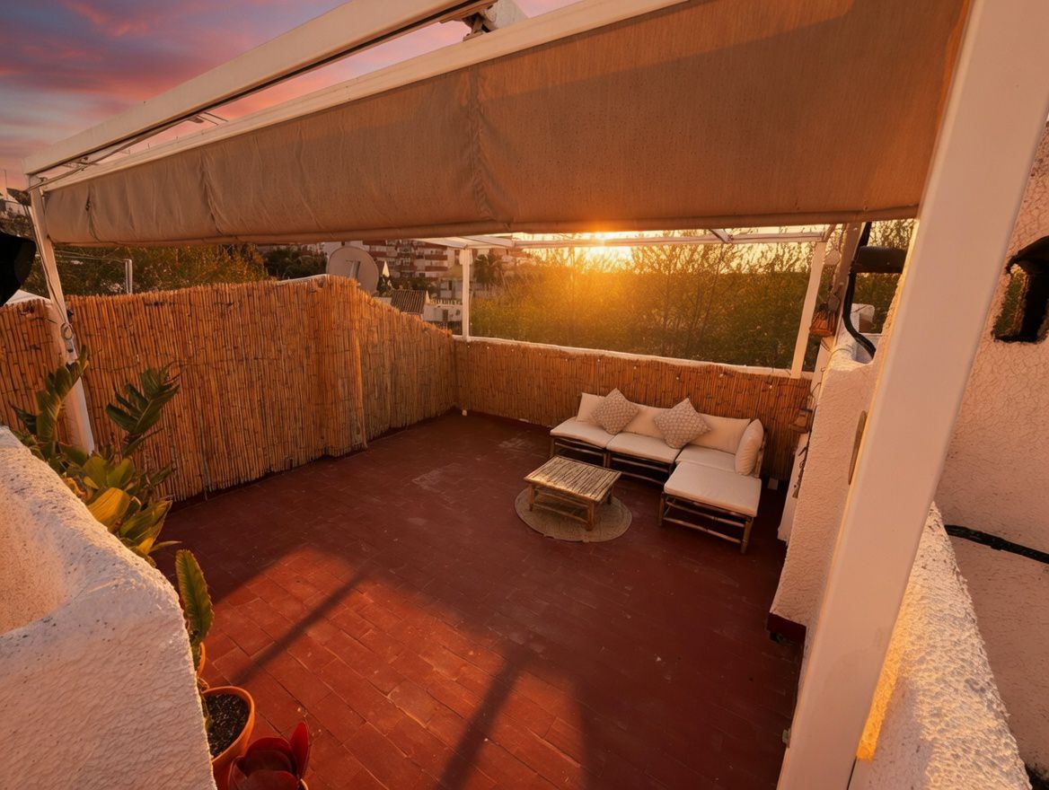 Private Terrasse mit Markise, rotem Fliesenboden und Bambuszaun. Mit Gartenmöbeln und Blick auf den Sonnenuntergang.