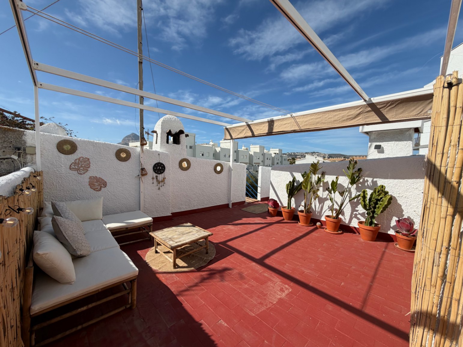 Sonnige Terrasse mit Terrakottaböden, Bambussofa und Topfpflanzen, ideal für den Genuss im Freien.